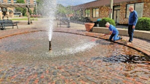 Ironton Rotary Club sergeant at arms Jeff Clark uses a rake to try to get a deflated birthday balloon out of the fountain as Carl Darling looks on. Club members were cleaning up the area around Rotary Park on Saturday in preparation of the upcoming Ironton-Lawrence County Memorial Day Parade. (The Ironton Tribune | Mark Shaffer)