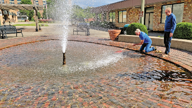Ironton Rotary Club sergeant at arms Jeff Clark uses a rake to try to get a deflated birthday balloon out of the fountain as Carl Darling looks on. Club members were cleaning up the area around Rotary Park on Saturday in preparation of the upcoming Ironton-Lawrence County Memorial Day Parade. (The Ironton Tribune | Mark Shaffer)